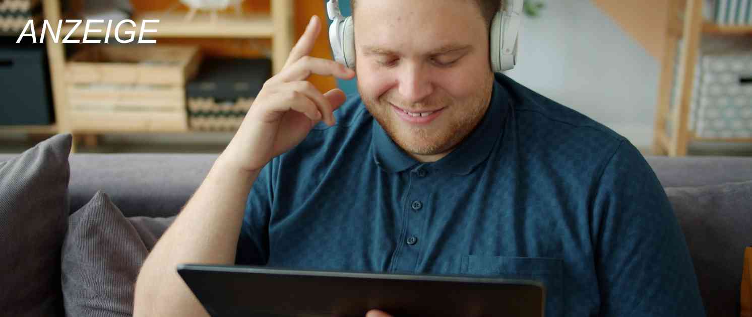 Mann sitzt auf der Couch am Laptop und hat Kopfhörer auf
